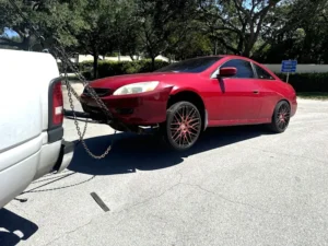 Red car with elevated front end being towed by a white truck, representing sell your junk car in Kendall FL services