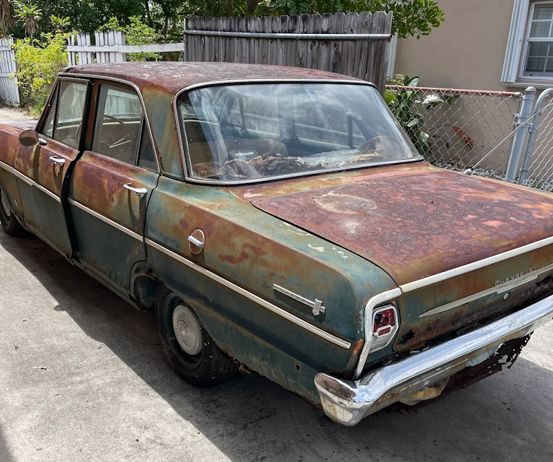 A heavily rusted vintage Chevrolet sedan parked on a driveway, ready for a junk old car buyer in Pompano Beach to haul it away.