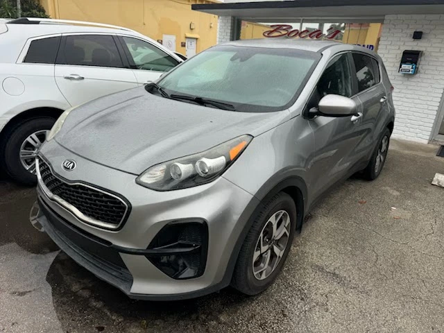 A silver Kia Sportage parked in front of a repair shop, illustrating the process to sell a non-running Kia Sportage in Boca Raton.