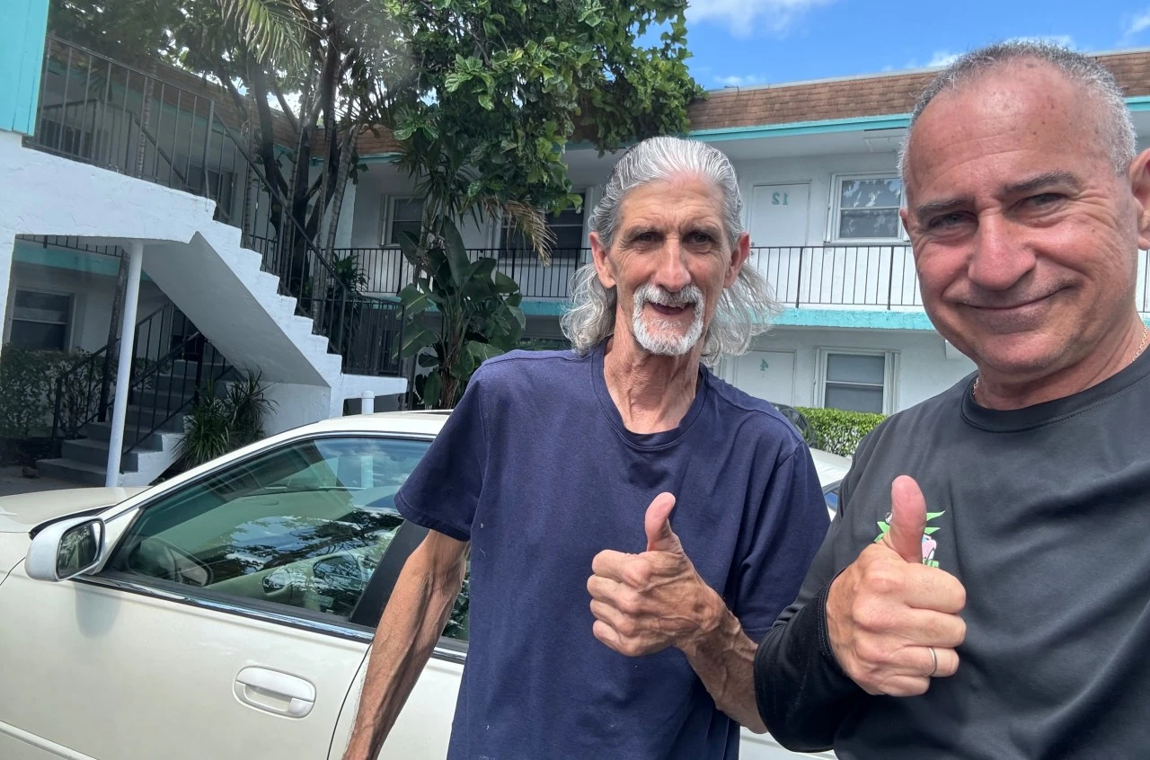 Two men giving a thumbs-up in front of an old white sedan after choosing to sell to a junk car service vs Facebook Marketplace in Fort Lauderdale.