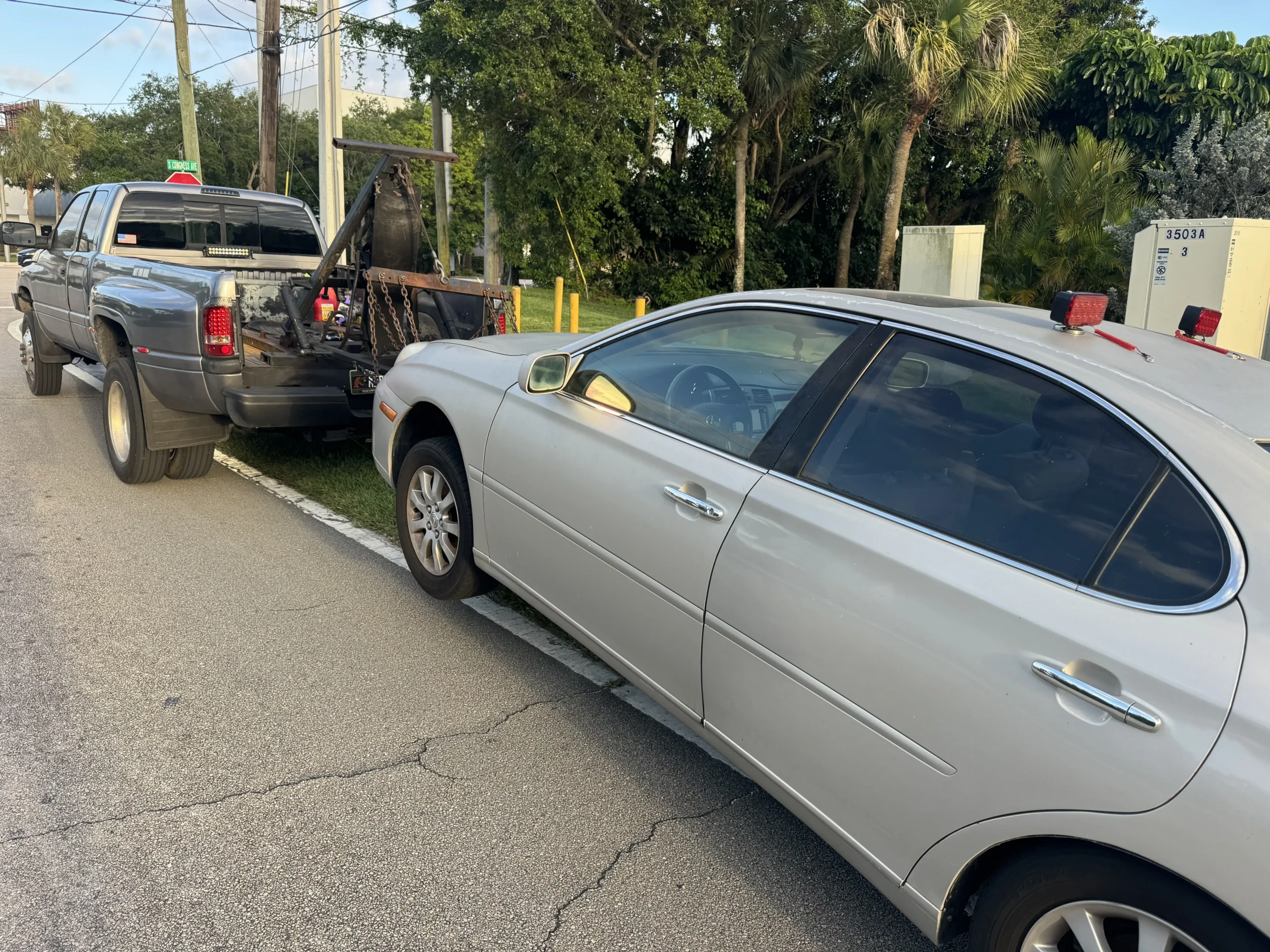 Tow truck hauling away a dark Volvo sedan during a free junk car pickup in Broward County