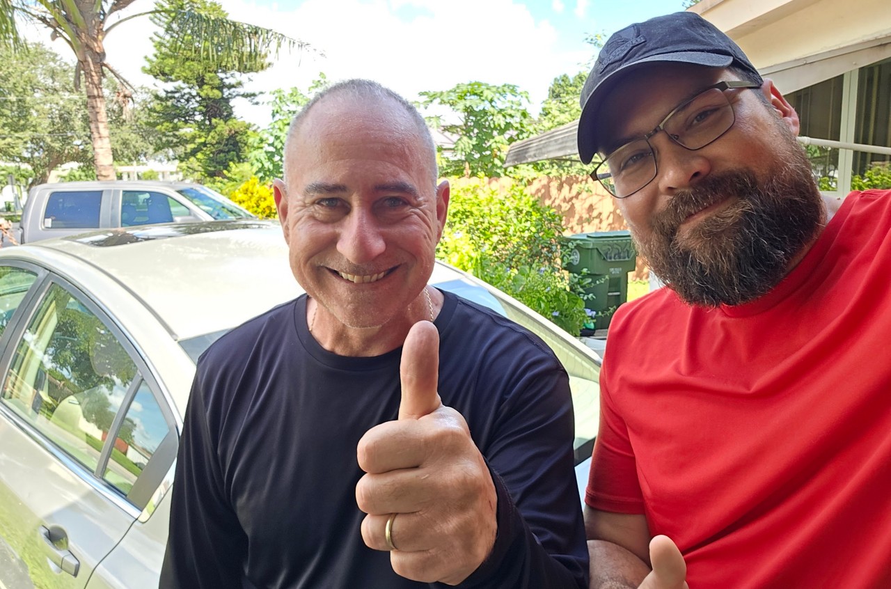 A man giving a thumbs-up next to a seller after deciding whether to repair a flooded engine or sell car for cash.