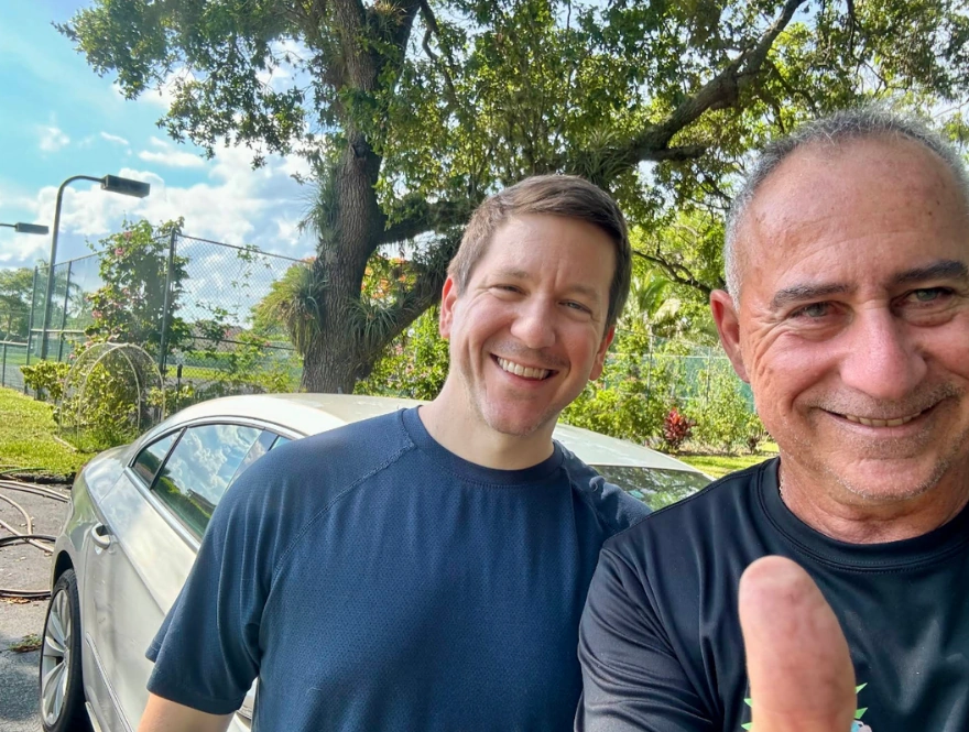 Two men smiling outdoors beside a vehicle while discussing how to sell a junk car without wheels with Hercules Buys Junk Cars.
